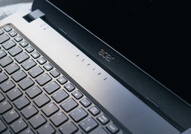 Refurbished Acer laptops collection banner showing a close-up, low-angle view of an open laptop with a vibrant blue backlit keyboard in a dark setting.