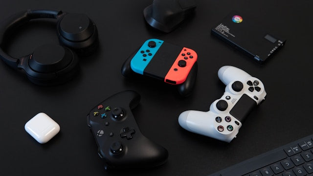 Popular refurbished electronics collection banner showcasing a flat lay of high-demand tech gear including headphones, an Apple Magic Mouse, and Nintendo Switch Joy-Cons on a dark surface.