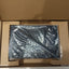 A black Lenovo laptop inside its  brown cardboard packaging box, still wrapped in protective plastic.