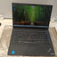 A black Lenovo ThinkPad laptop on a white surface, partially wrapped in protective plastic. The screen is turned on, and the keyboard, trackpad, and red TrackPoint nub are clearly visible.